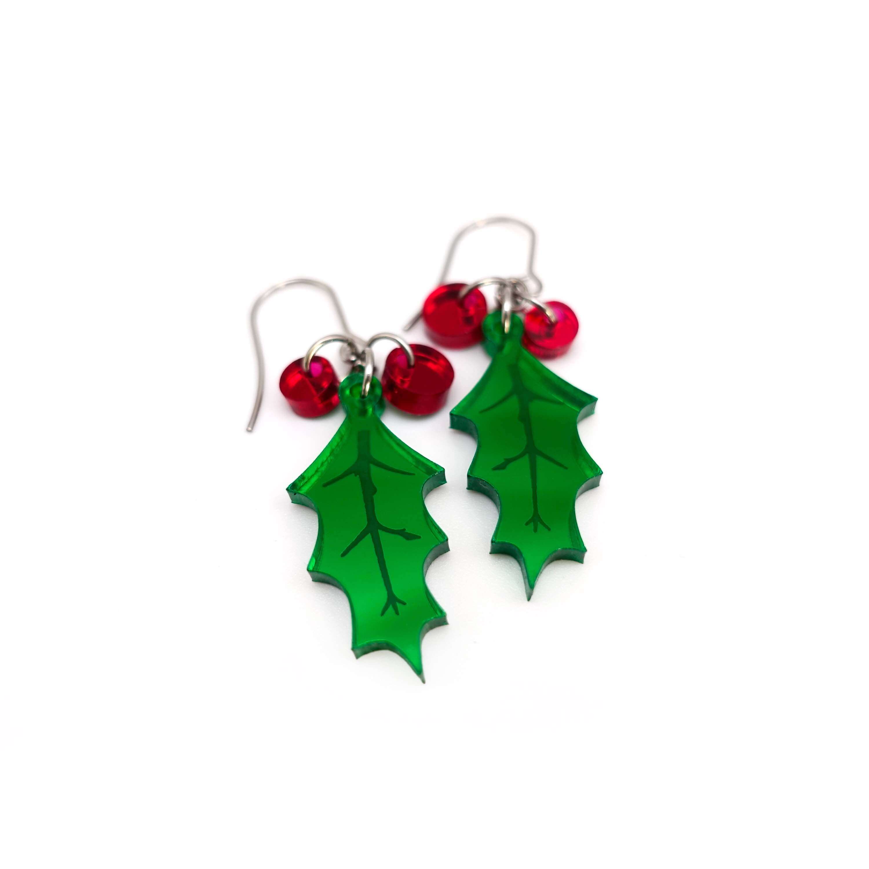 A pair of naturalistic Holly earrings with red berries shown lying on a white surface. 