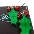 A close up of the delicate holly earrings with red berries on stainless steel ear wires sitting on a Wear and Resist gift box. 