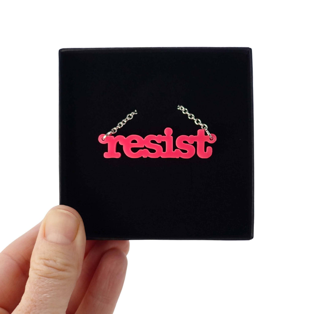 Hot pink Resist necklace in typewriter font shown in a Wear and Resist gift box. 