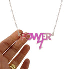 Mini power necklace in iridescent shown hanging on a silver chain against a white background. Designed in collaboration with Mary Beard for her book Women and Power. 
