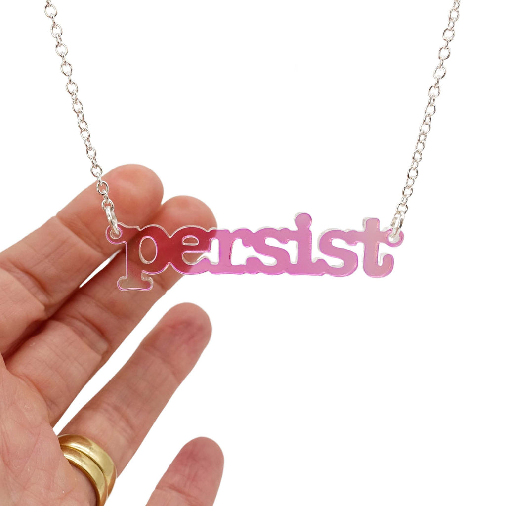 Iridescent Persist necklace in typewriter font hanging on a silver chain against a white background. 
