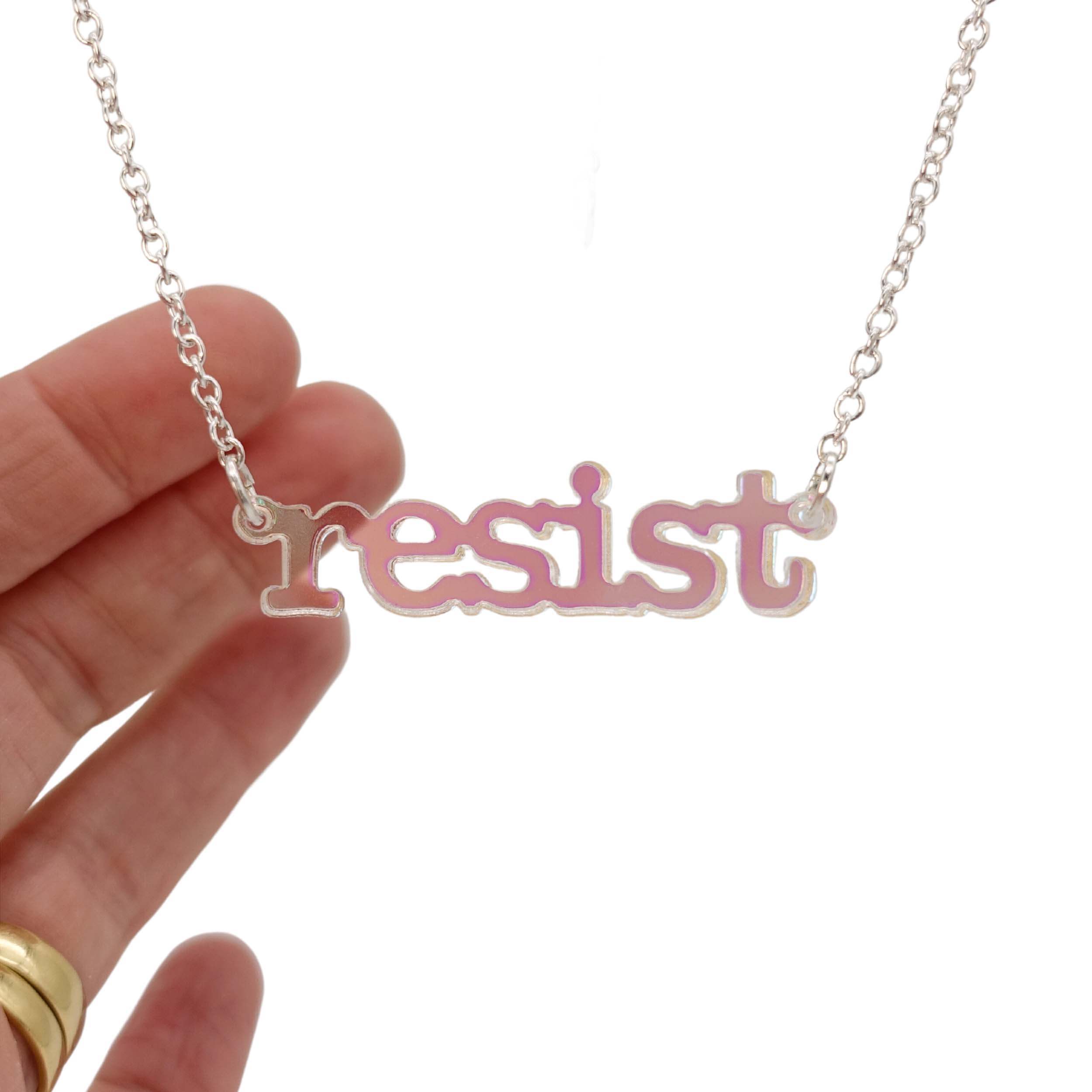 Iridescent Resist necklace in typewriter font hanging on a silver chain against a white background. 