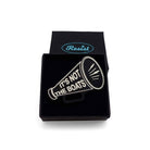 A matte black acrylic brooch in the shape of a megaphone etched in glow-in-the-dark pigment with the words 'It's not the boats', shown in a small Wear & Resist gift box.