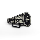 A matte black acrylic brooch in the shape of a megaphone etched in glow-in-the-dark pigment with the words 'It's not the boats', shown on a white background.