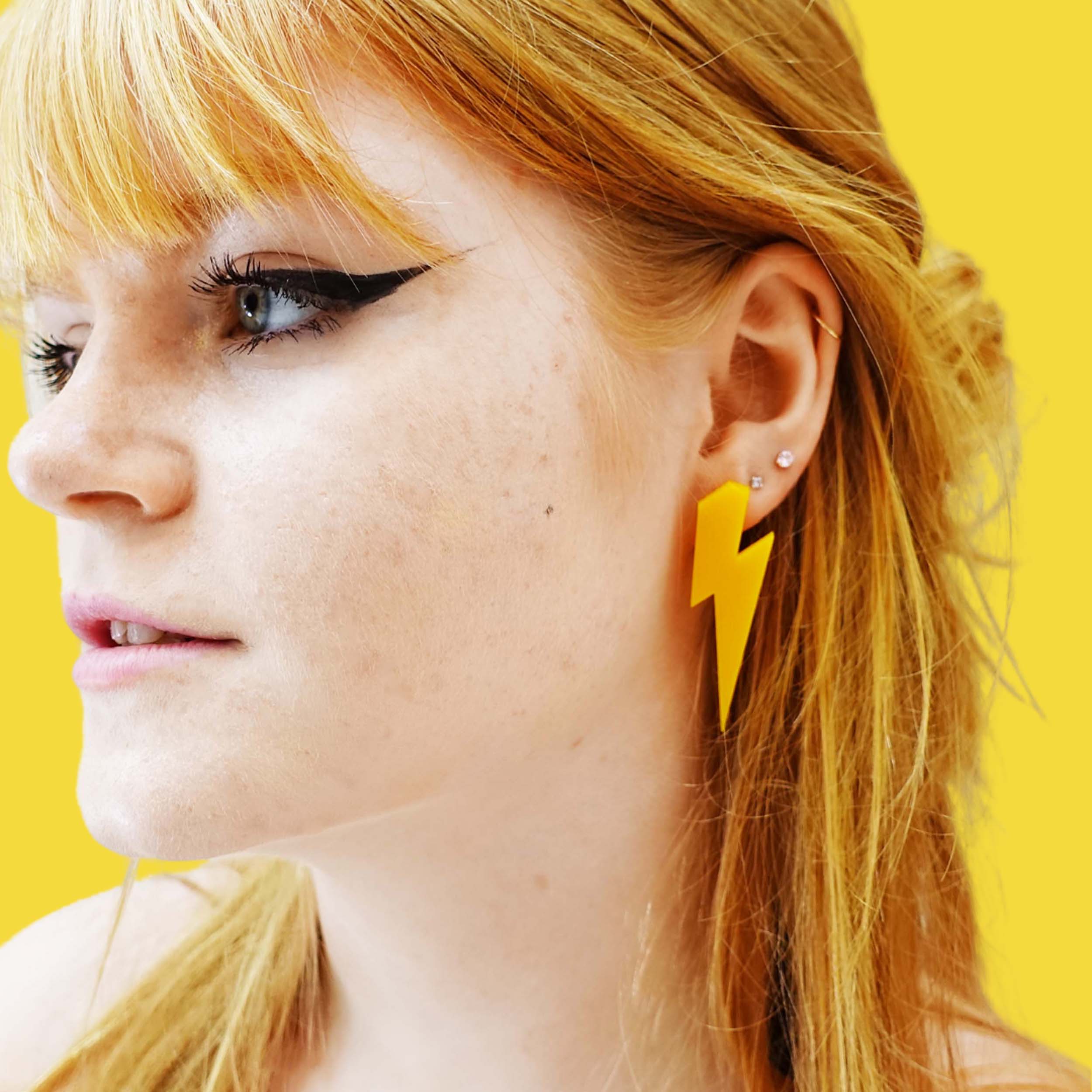 Eliza wears sunflower yellow large colour-pop Lightning Bolt earrings, designed by Sarah Day for Wear and Resist. 