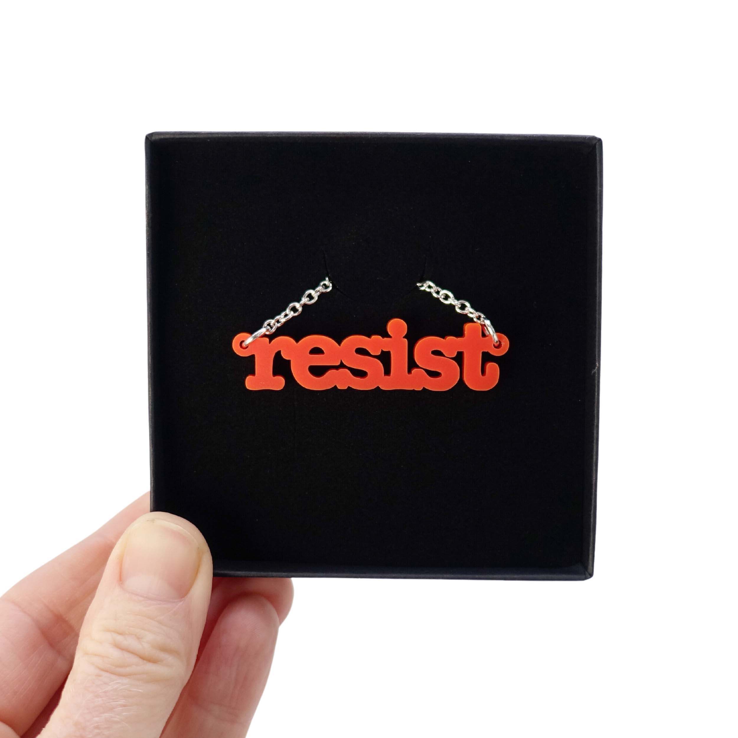 Matte red Resist necklace in typewriter font shown in a Wear and Resist gift box. 