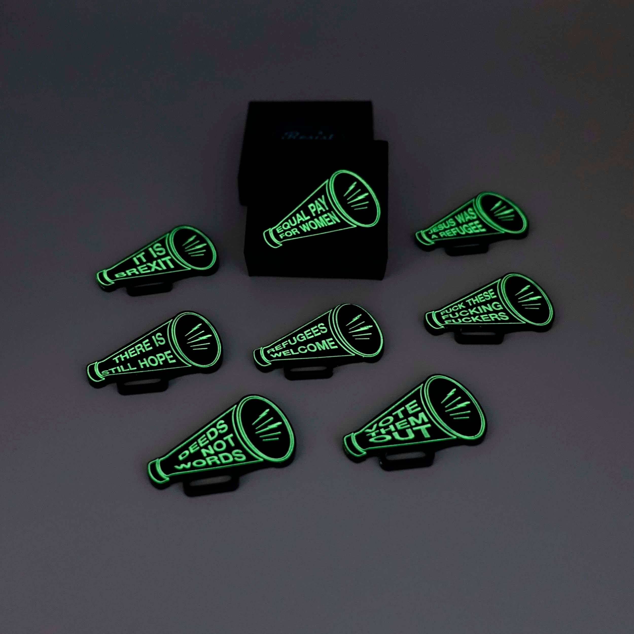 A group of Megaphone brooches shown glowing in the dark alongside a Wear and Resist gift box