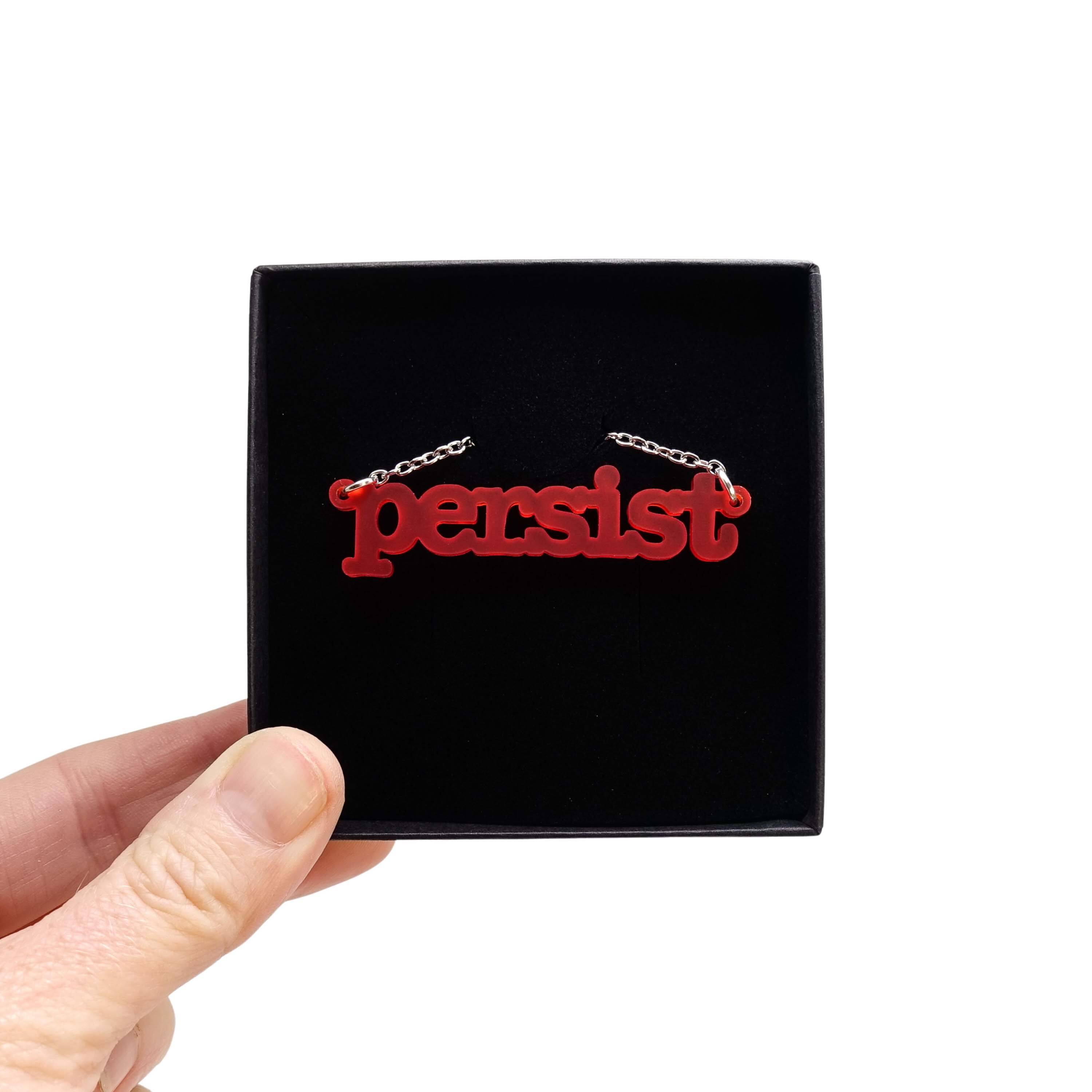 Typewriter Resist necklace in chilli frost shown held up in a Wear and Resist gift box.
