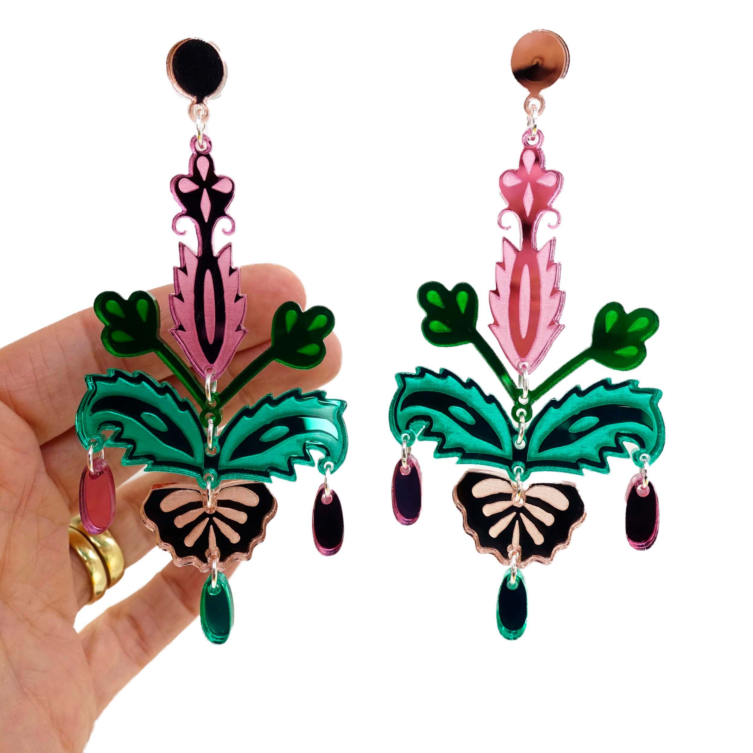 Pink and green festive drop statement earrings shown with a hand behind. 