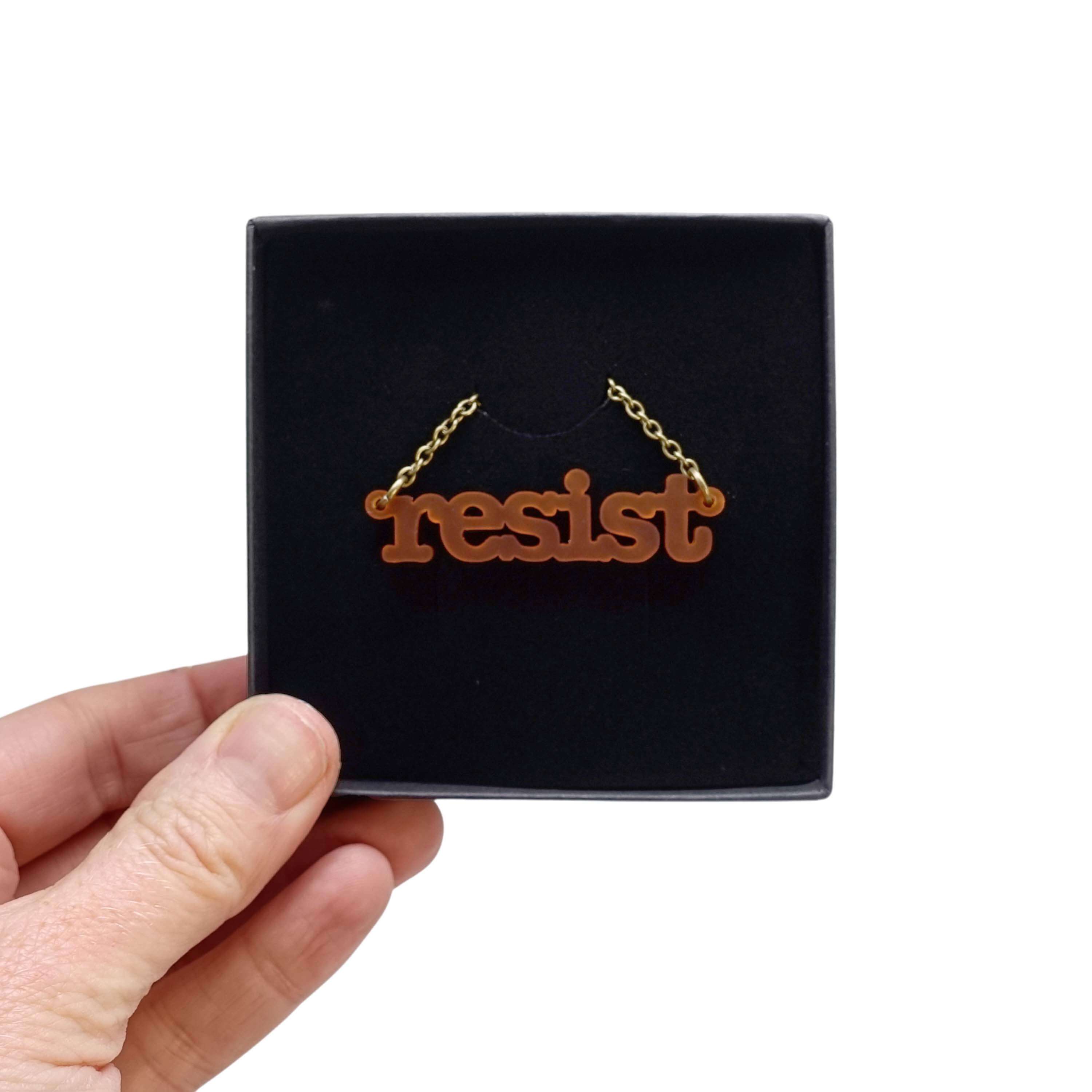 Typewriter Resist necklace in cider frost shown held up in a Wear and Resist gift box. 