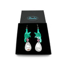A pair of acrylic earrings with green birds holding silver 'jewels' that say 'Nah' and 'Nope'. Shown in a Wear & Resist gift box. 