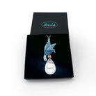 An acrylic pendant necklace with a blue bird holding a silver 'jewel' that says 'Nah.' Shown in a Wear & Resist gift box. 
