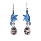 A pair of acrylic earrings with blue birds holding silver 'jewels' that say 'P*ss Off'.