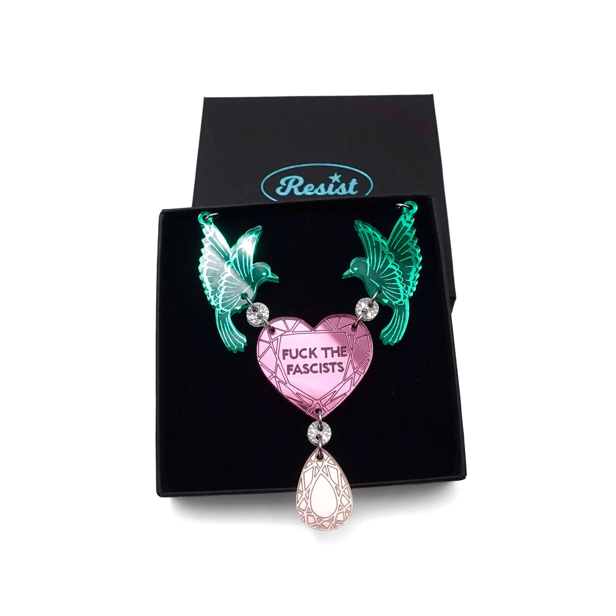 A mirror acrylic necklace with two green birds holding a pink heart that says 'Fuck the Fascists' with a rose gold 'jewel' hanging from the centre, shown in a Wear and Resist gift box. 