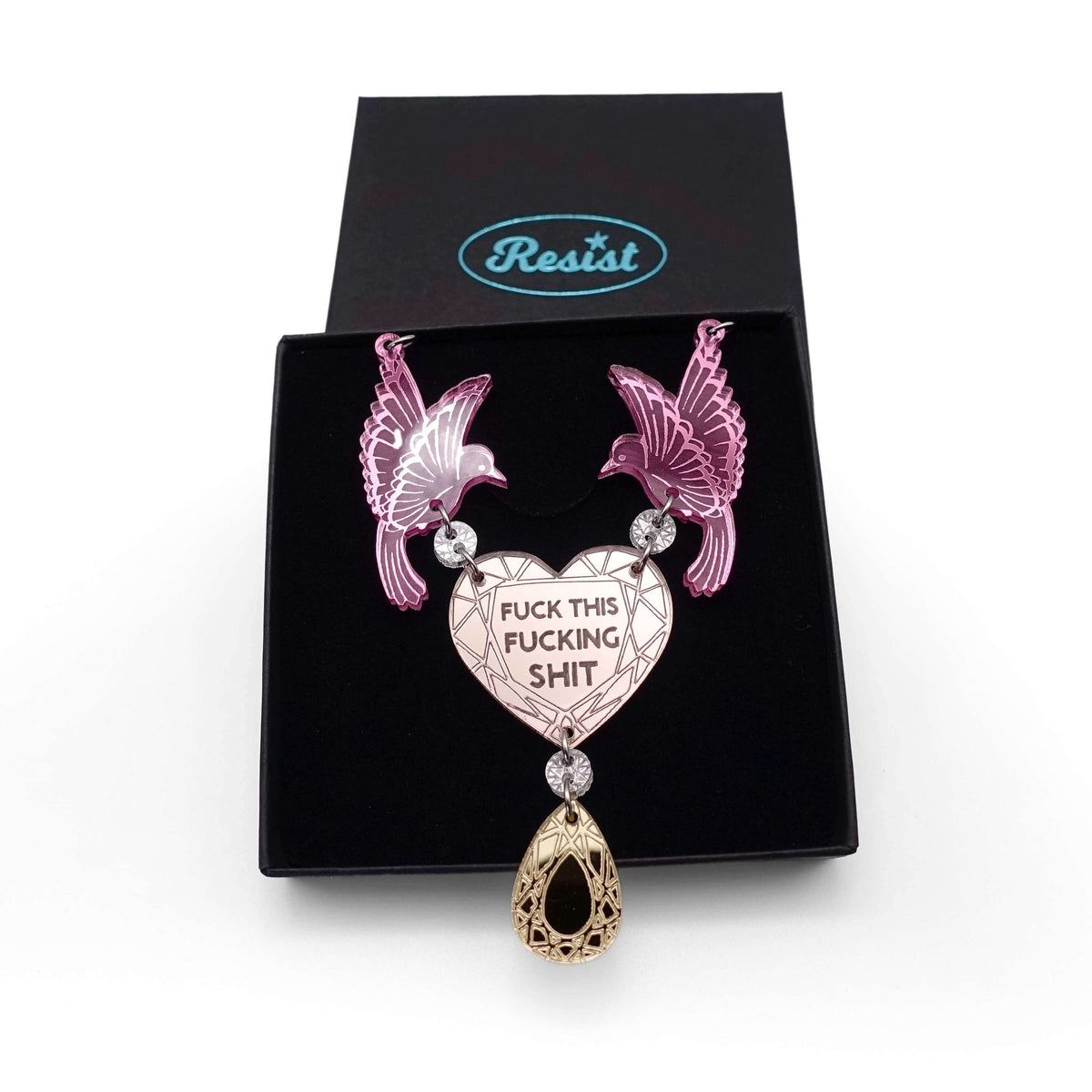 A mirror acrylic necklace with two pink birds holding a rose gold heart that says 'Fuck this fucking shit' with a gold 'jewel' hanging from the centre. Shown in a Wear and Resist gift box. 