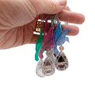 My hand holding a group of Rude Bird pendant necklaces in blue, pink and green, with sweary silver 'jewels' 