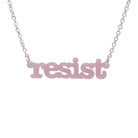 Shell pink Resist necklace in typewriter font hanging on a silver chain against a white background. 