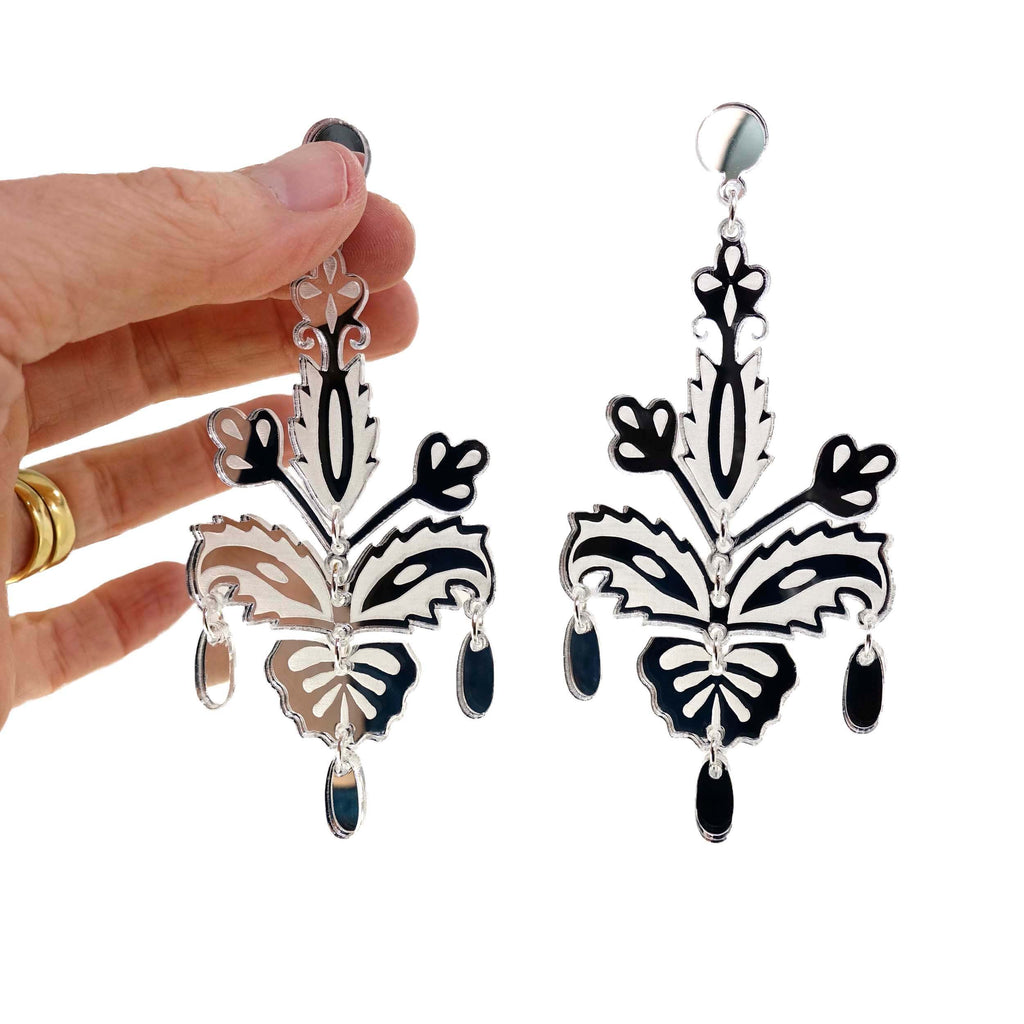 All silver festive drop statement earrings shown against a white background with a hand holding one. 