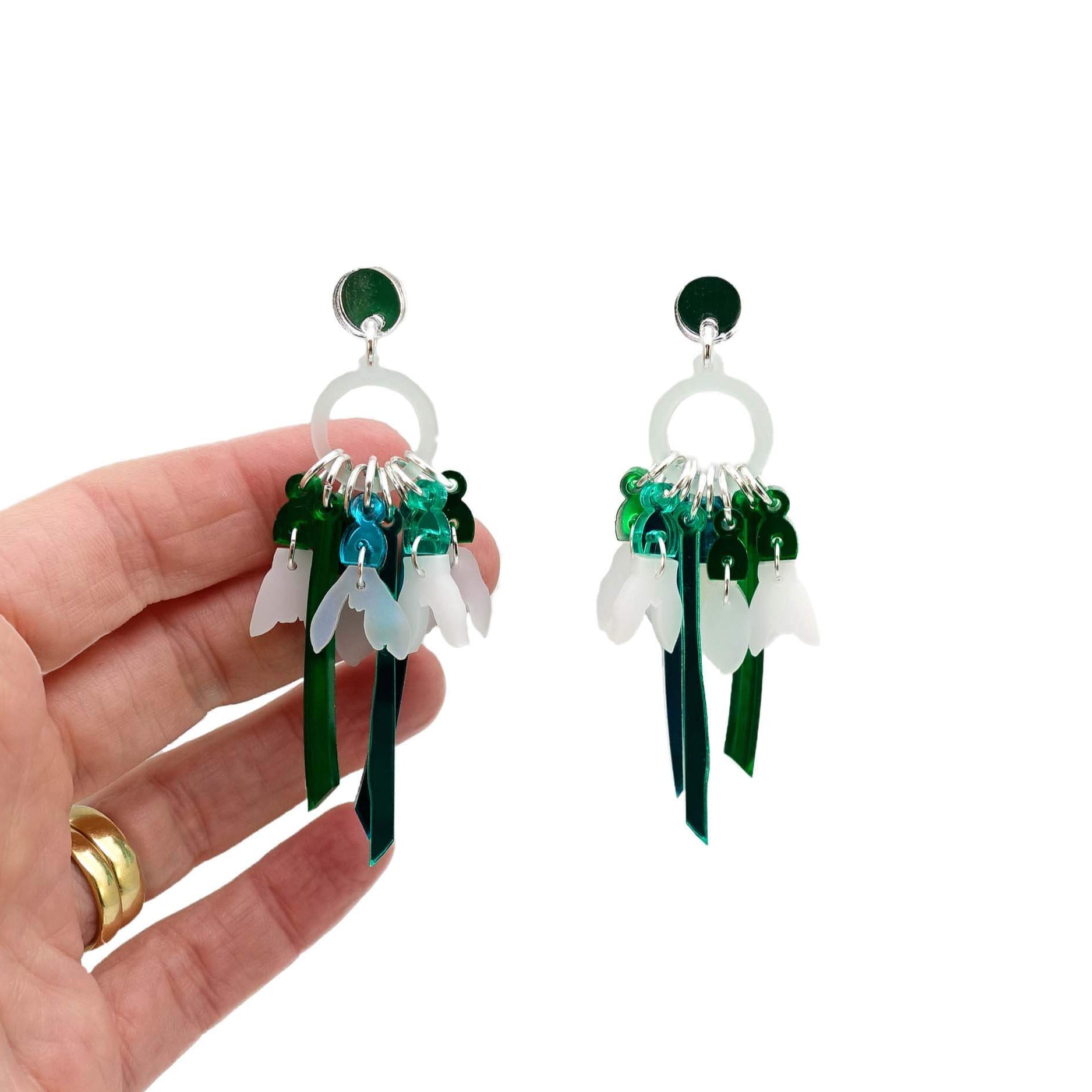 Snowdrop earrings shown hanging against a white background with my hand behind for scale. 