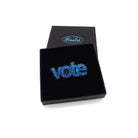 Vote brooch in blue glitter shown in a Wear and Resist gift box. 