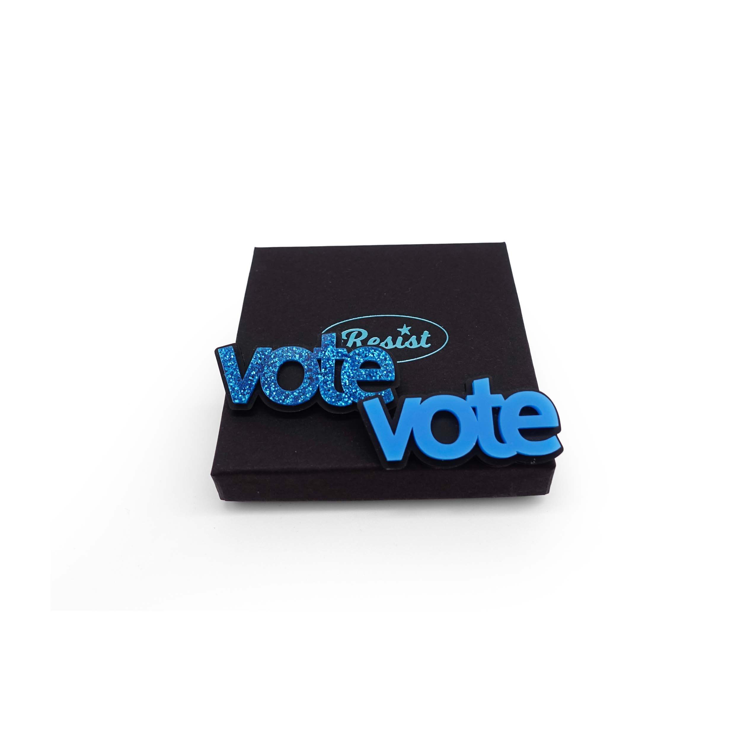 Vote brooches in blue glitter and bright matte blue shown on a Wear and Resist gift box. 