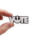 A matte white VOTE brooch with Rebel Alliance symbol from Star Wars, shown held up for scale. 