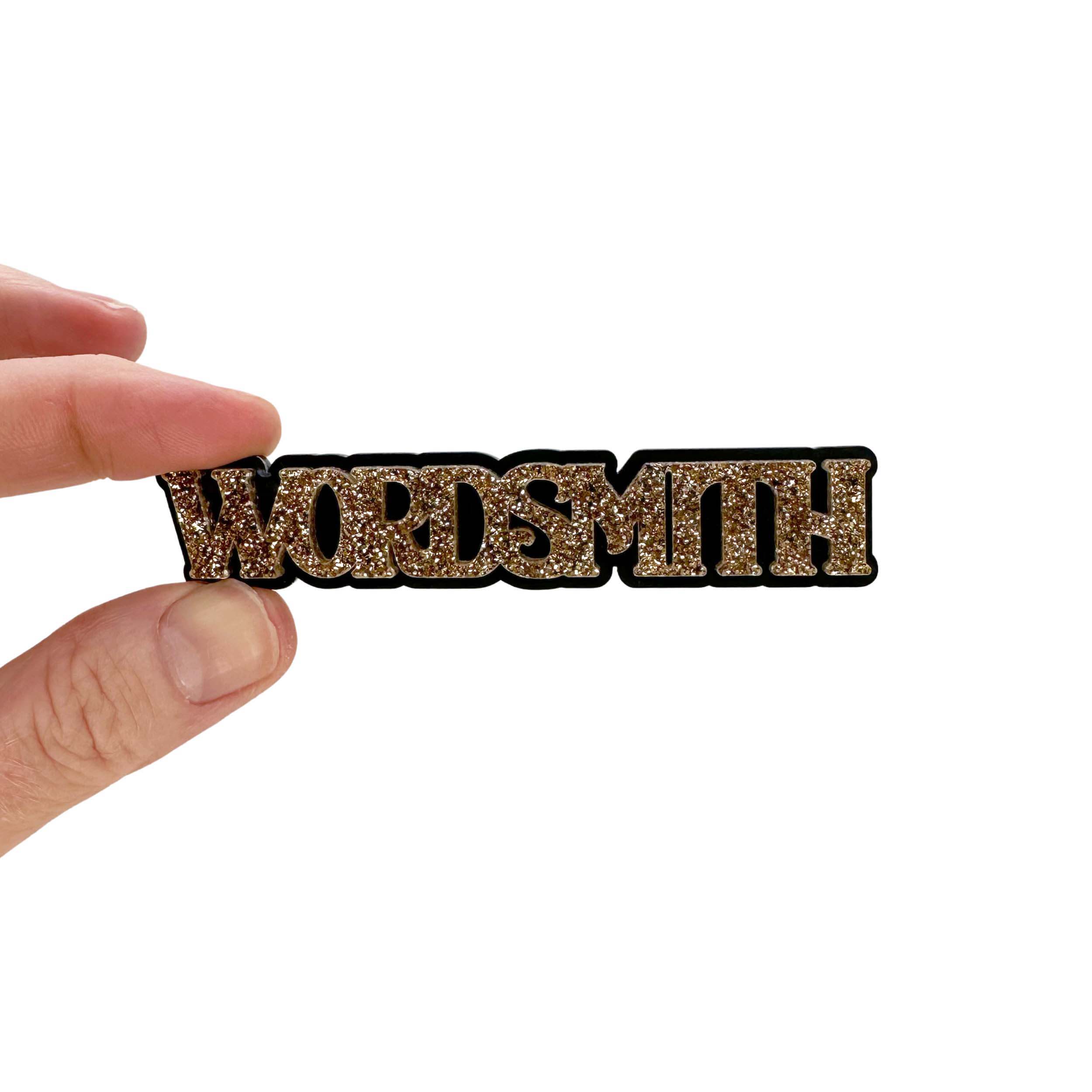 Wordsmith brooch in gold glitter shown held up against a white backround. 