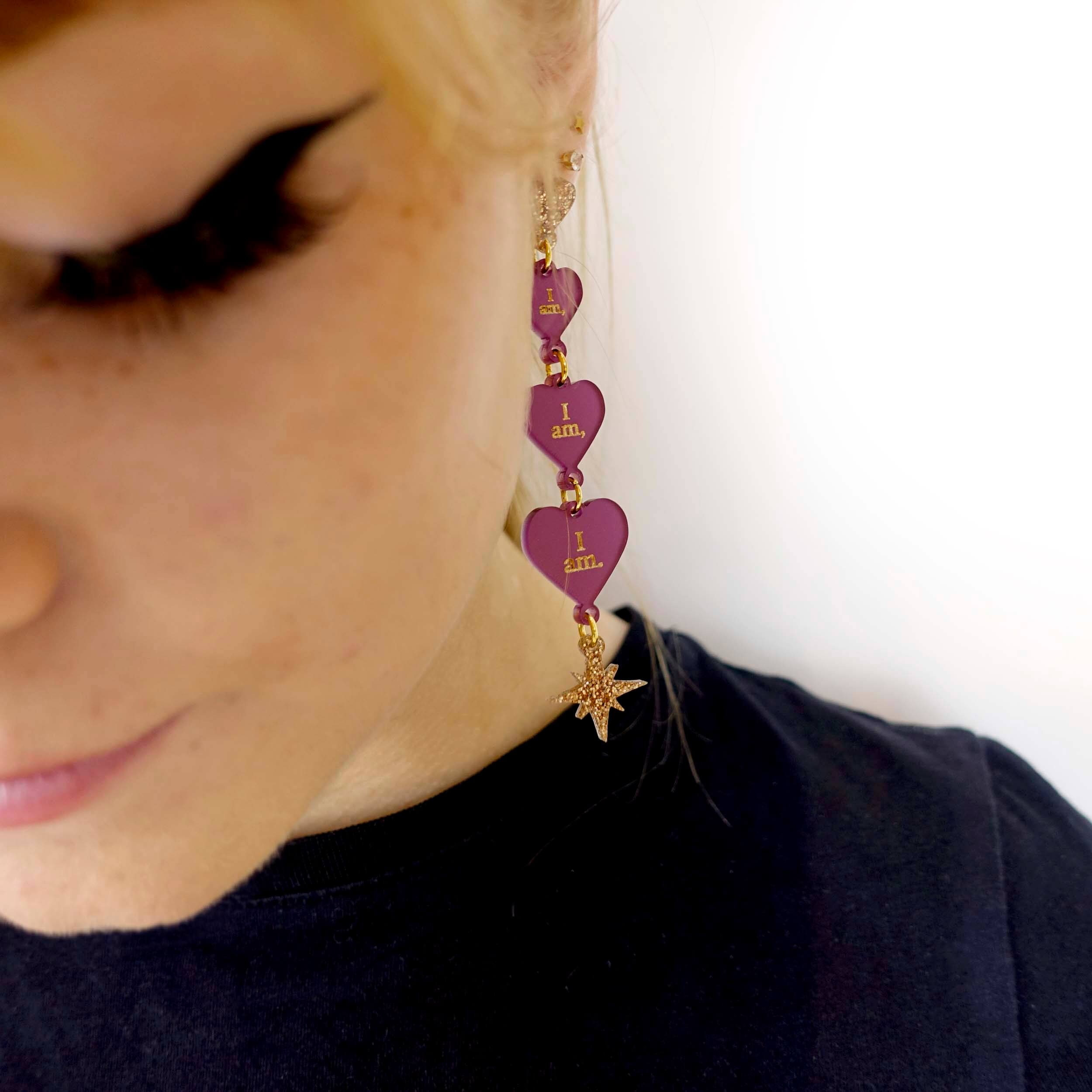 A close up of Eliza wearing I am I am I am engraved heart dangling earrings with gold vintage stars. 