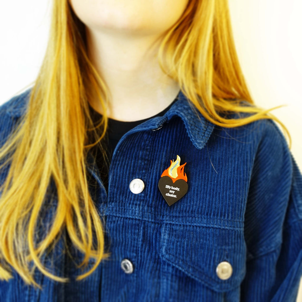 Model wears a My body my choice flaming heart brooch designed by Sarah Day for Wear and Resist. 