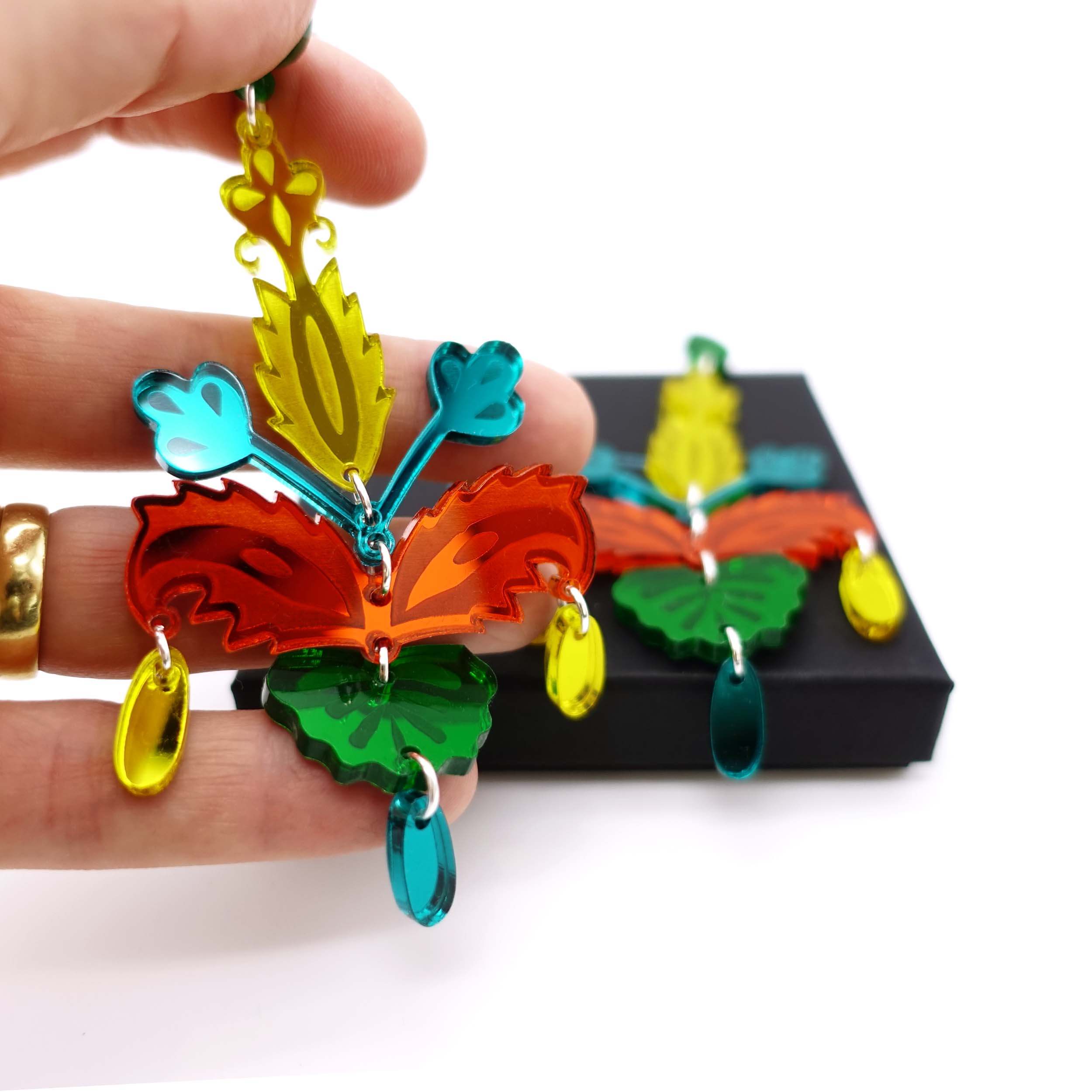 Yellow, teal, orange and green Mambo Festival statement earrings on Wear and Resist gift box and shown behind held up for size. 