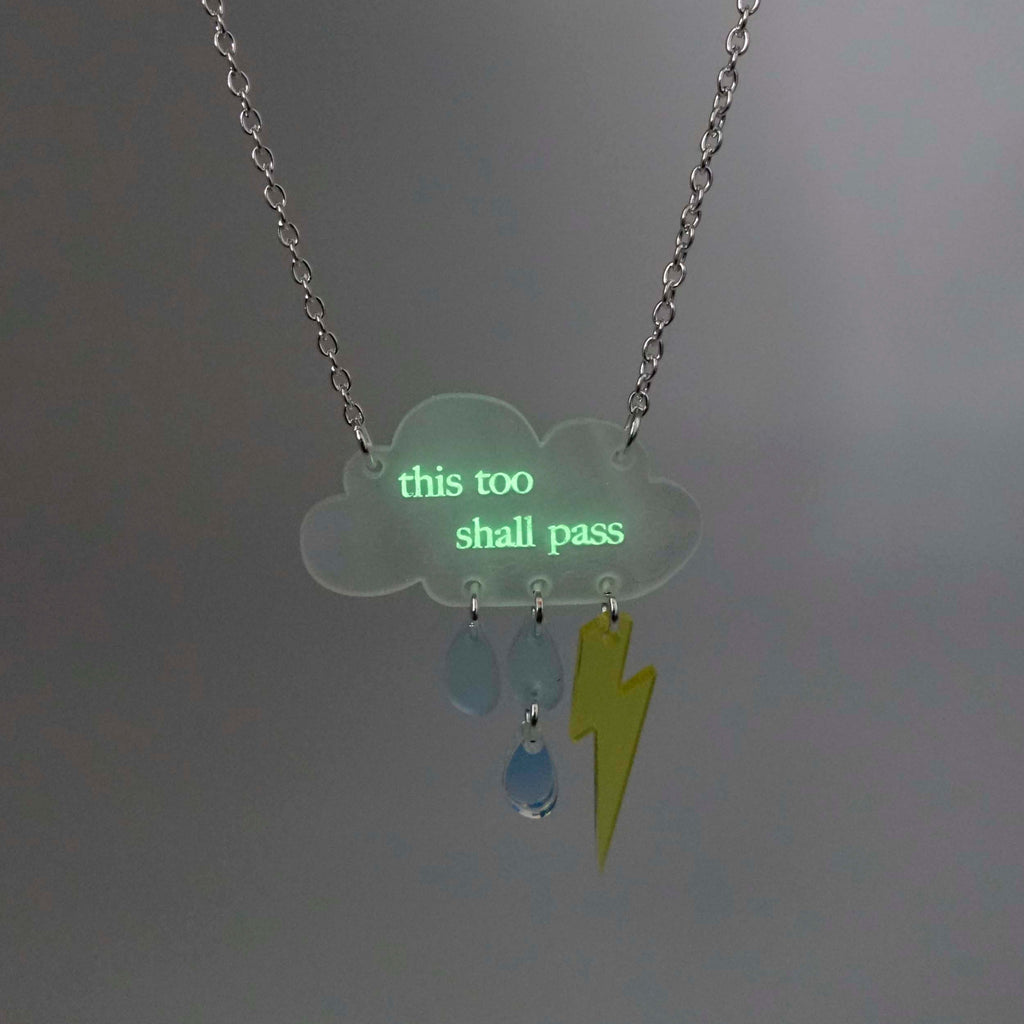 Glowing This too shall pass raincloud necklace, shown in dark light. 