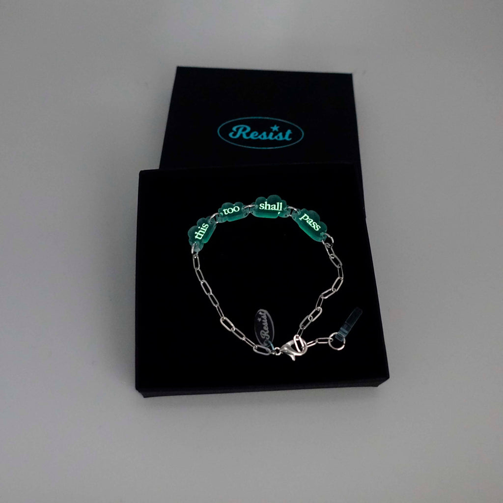 This too shall pass floating clouds silver-plated paperclip bracelet, etched with glow-in-the-dark pigment shown in a Wear and Resist gift box. 