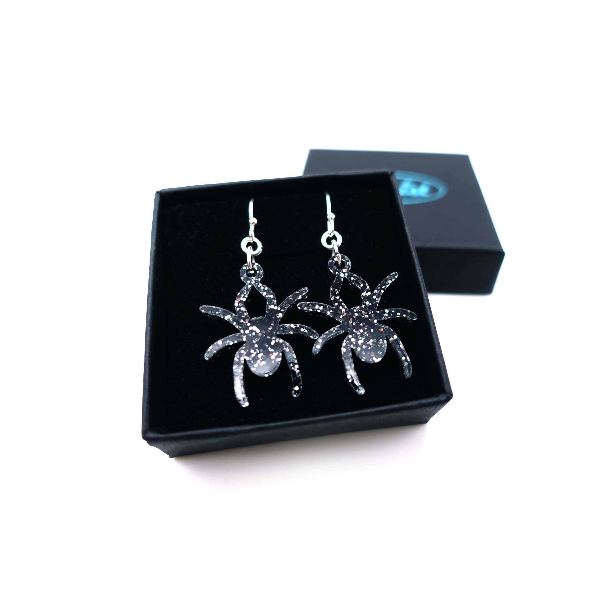 Lady Hale commemorative spider earrings in black glitter shown in box.