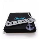 Courage necklace to benefit the RNLI and Women for Refugee Women in blue-grey with a slate mirror anchor etched with the words 'hold fast,' shown on gift box.