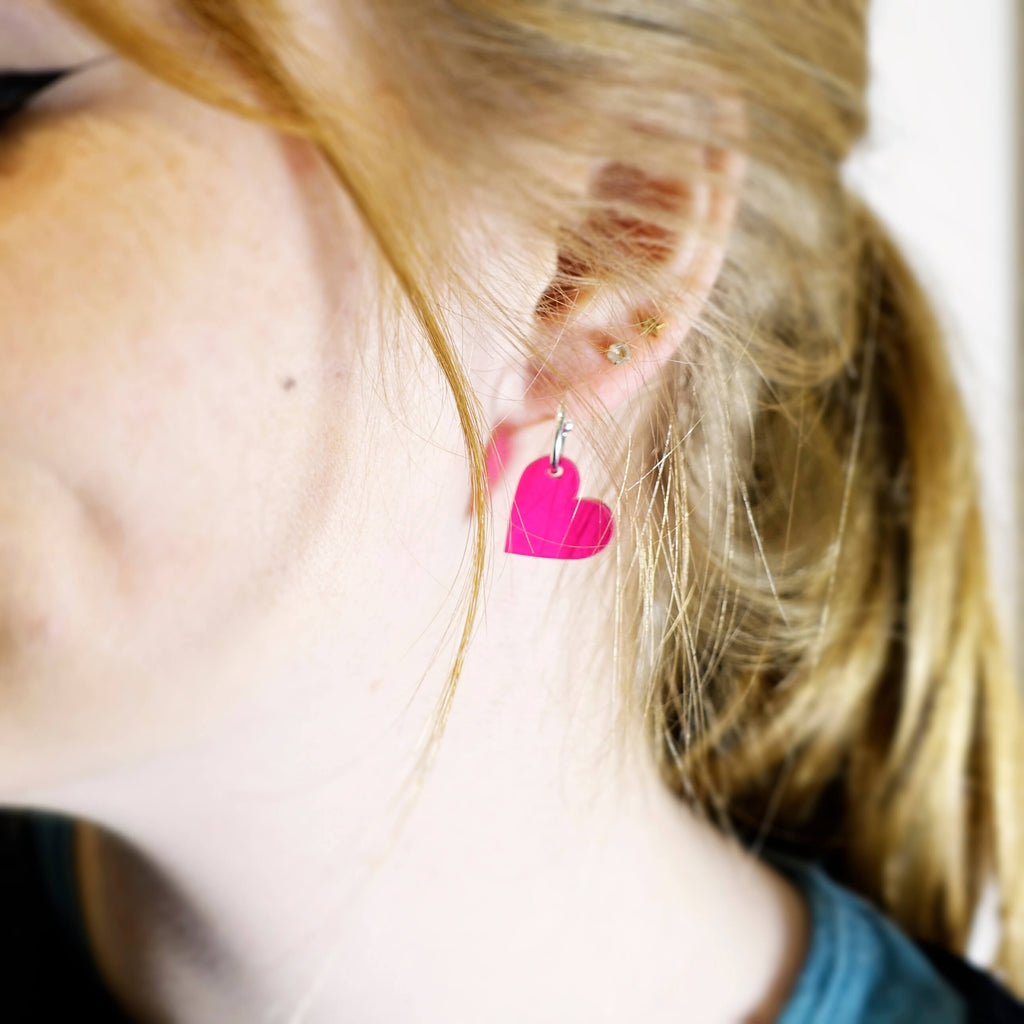 Eliza wears transparent hot pink simple heart hoop earrings. 