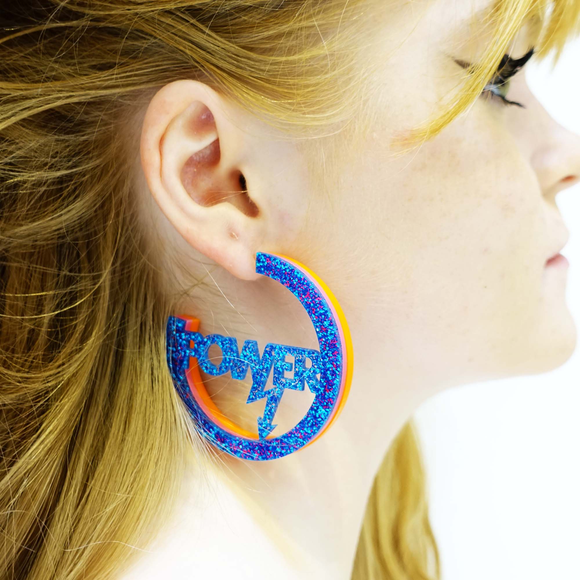 model wears hot glitter blue Mary Beard Women & Power earrings, statement hoops