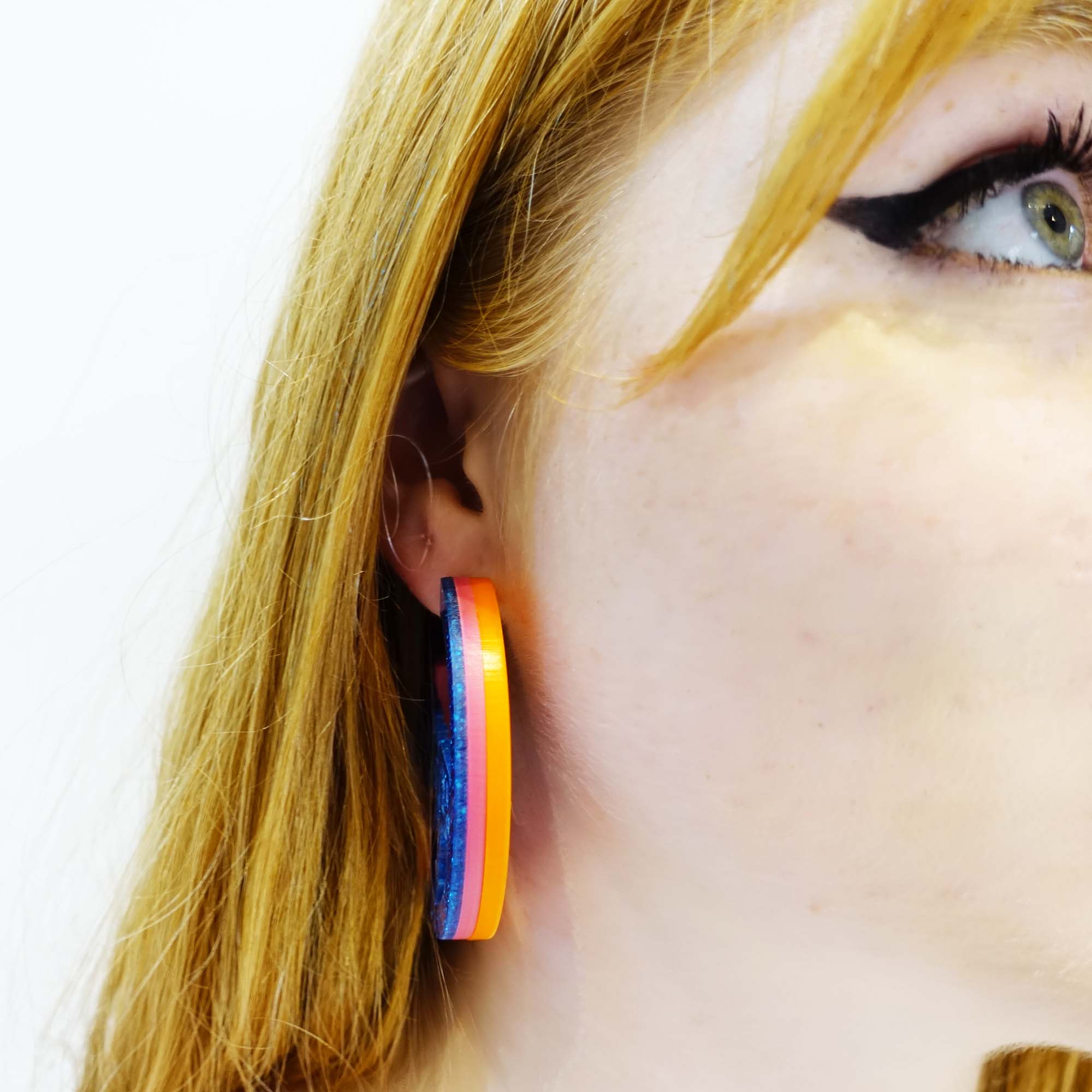 model wears hot glitter blue Mary Beard Women & Power earrings, statement hoops showing the bands of colour