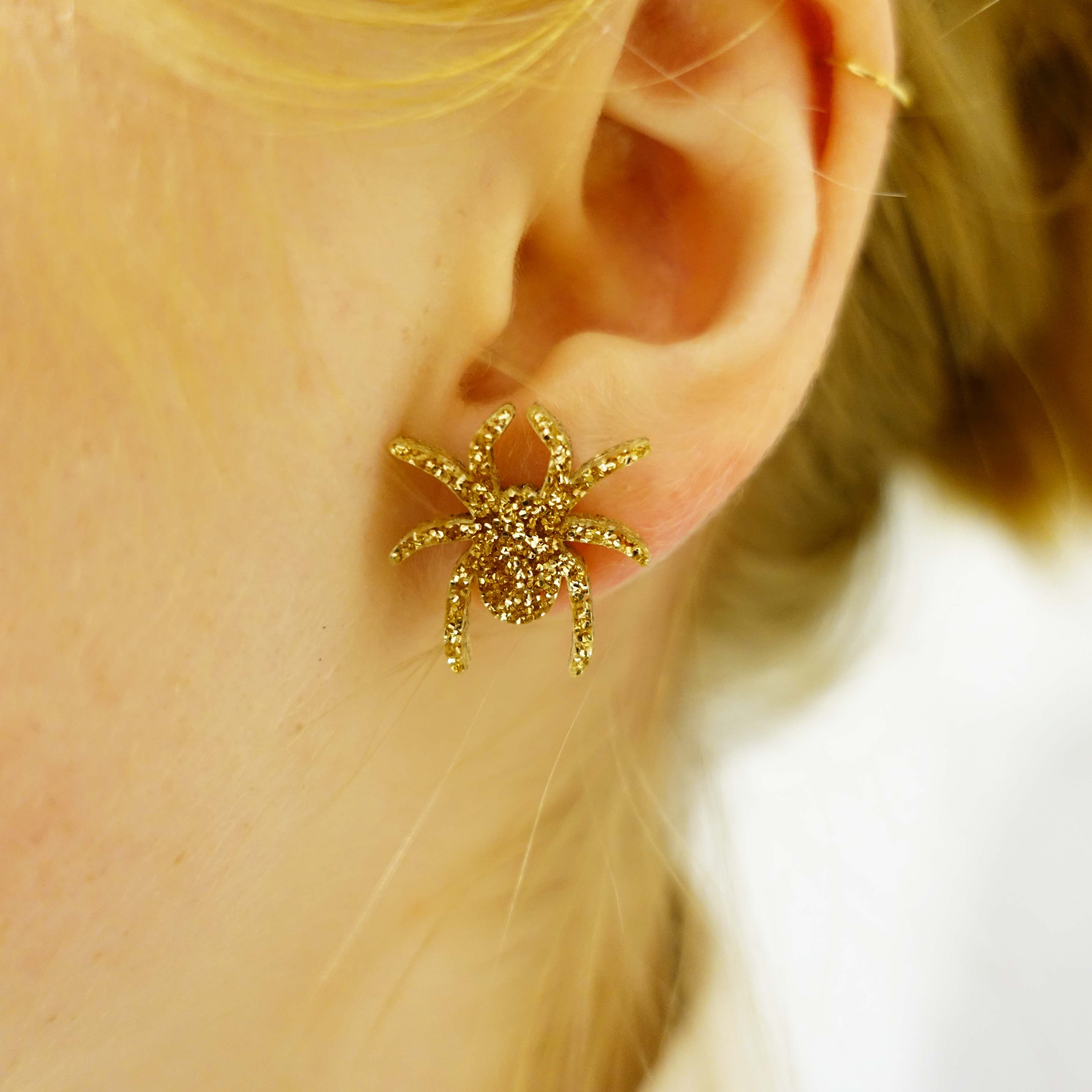 Model wears gold glitter Lady Hale spider stud earrings by Wear and Resist. 