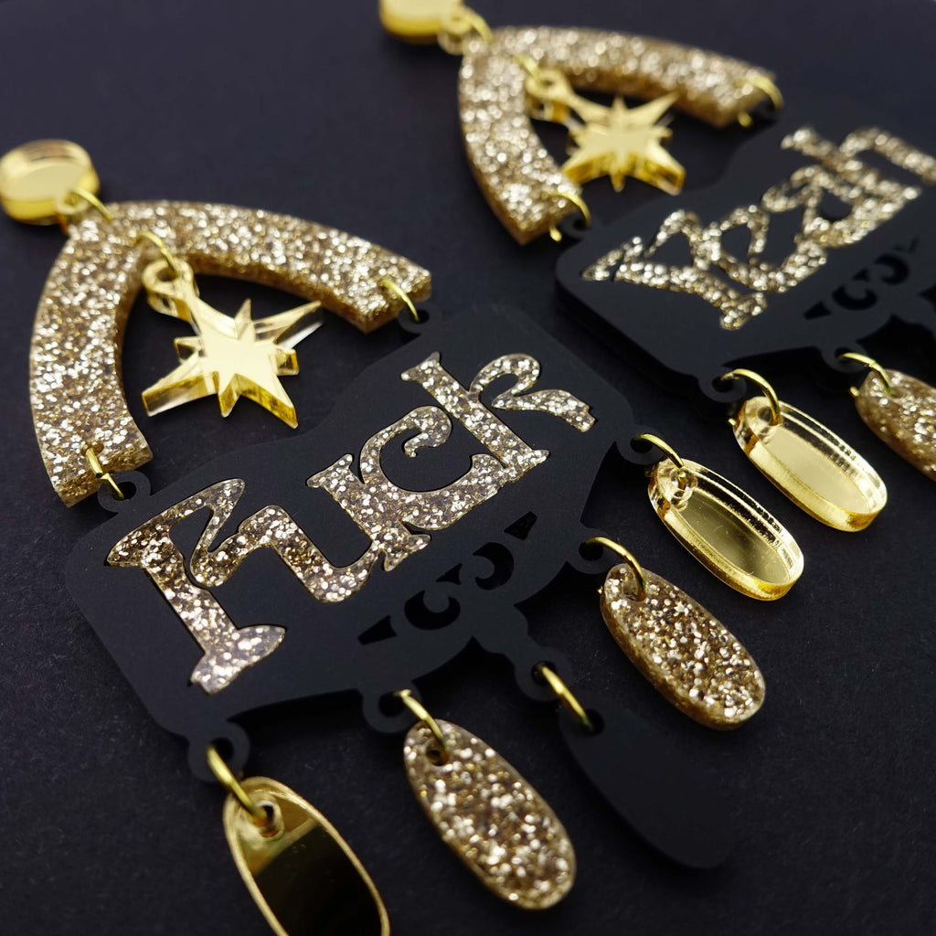 Fuck yeah earrings in black and gold glitter shown  in close up on black background
