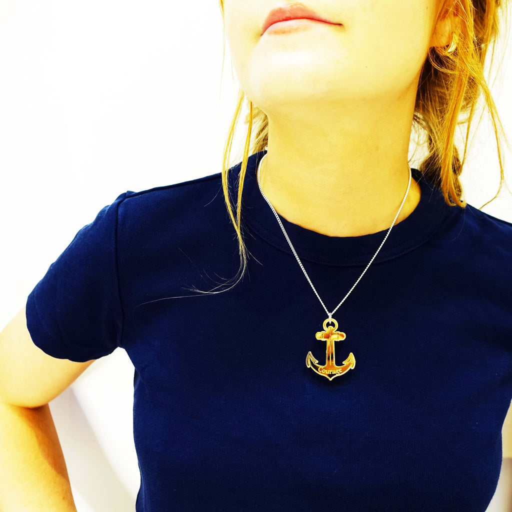 Model wears gold anchor pendant engraved with Courage in support of the RNLI and Women for Refugee Women