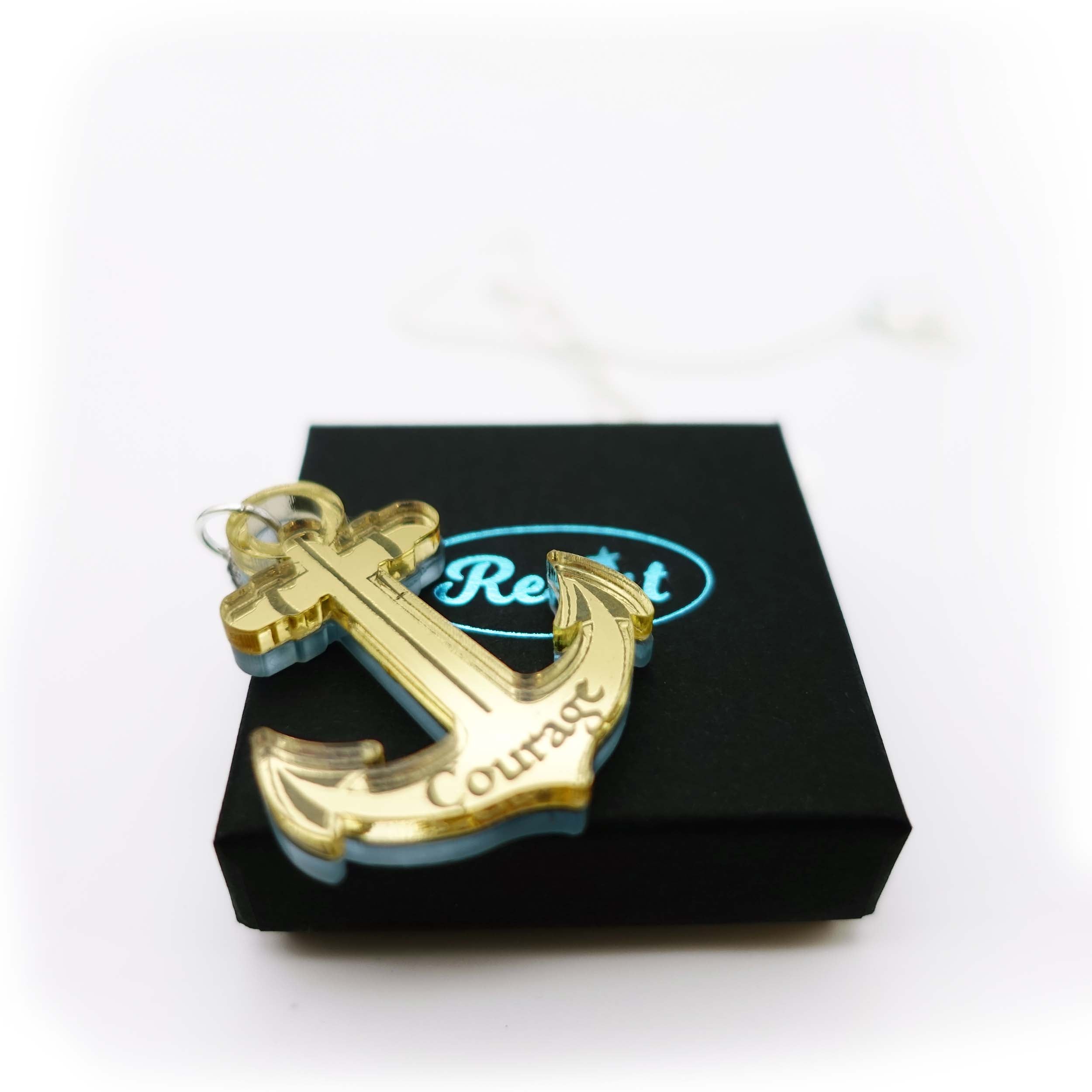Gold engraved courage anchor pendant shown on the small gift box. £4 from the sale of each will be split equally between the RNLI and Women for Refugee Women. 