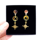 Warm gold Deco Star earrings shown in a Wear and Resist gift box, held up. 