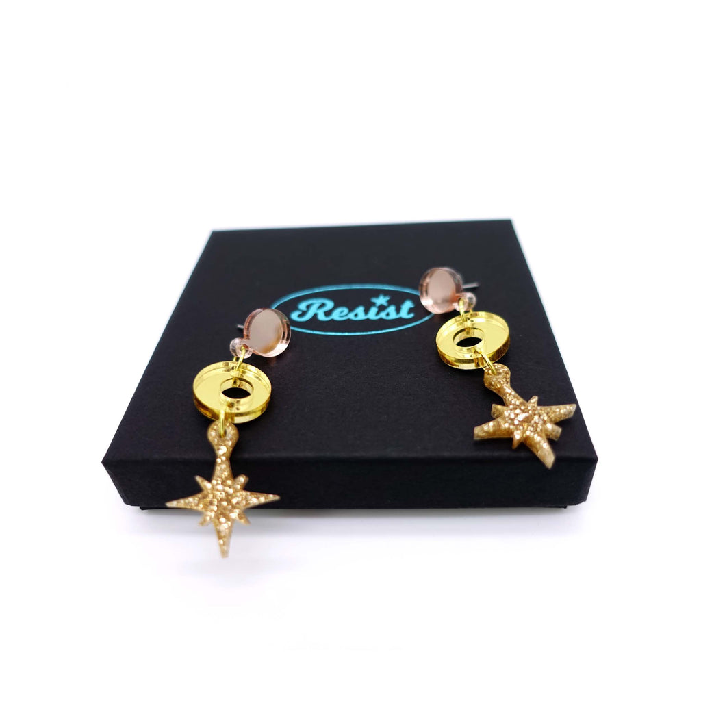 Warm gold Deco Star earrings shown on top of a Wear and Resist gift box. 