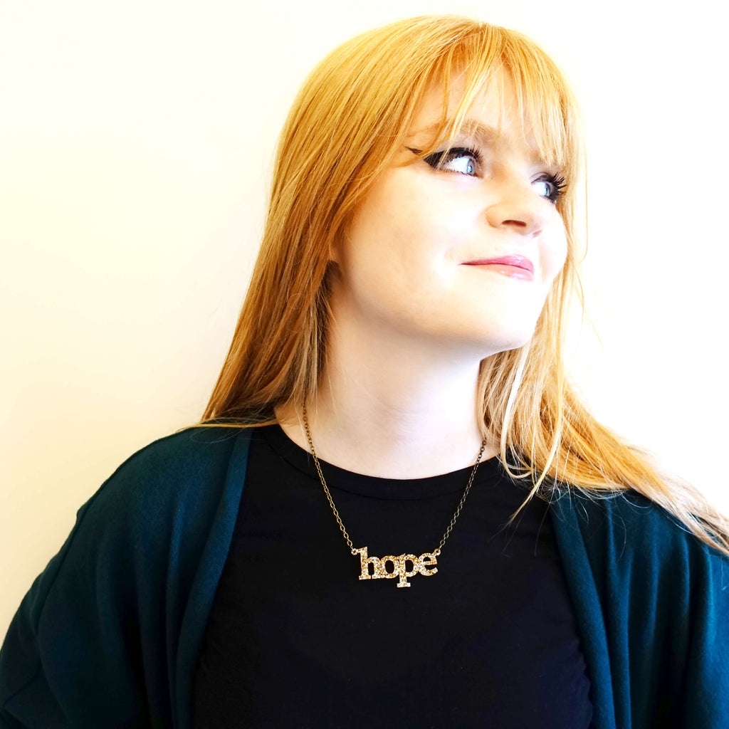 Model wears a gold glitter hope necklace designed by Sarah Day for Wear and Resist. 