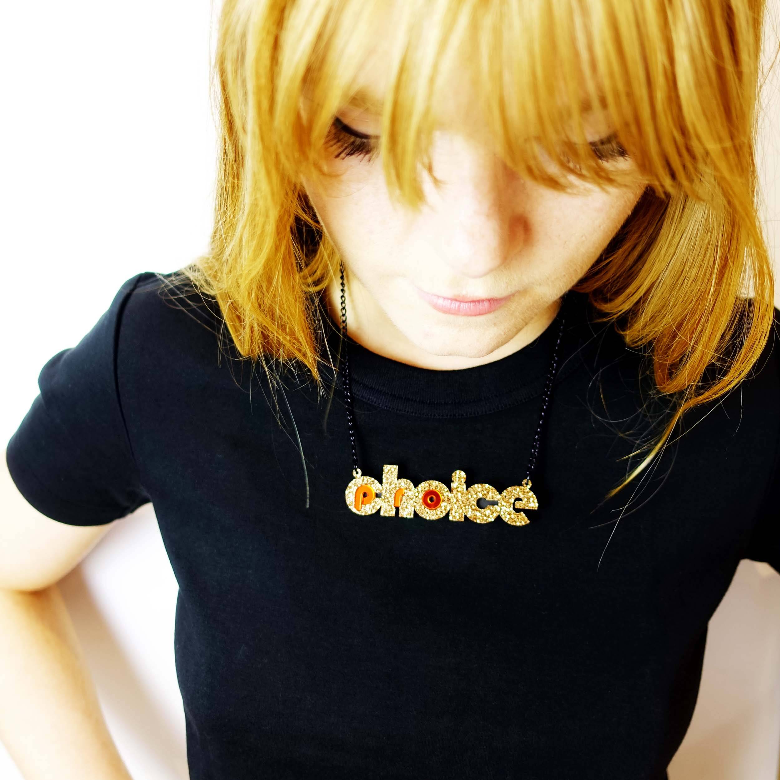 Model wears gold glitter pro-choice necklace, designed by Sarah Day for Wear and Resist. 