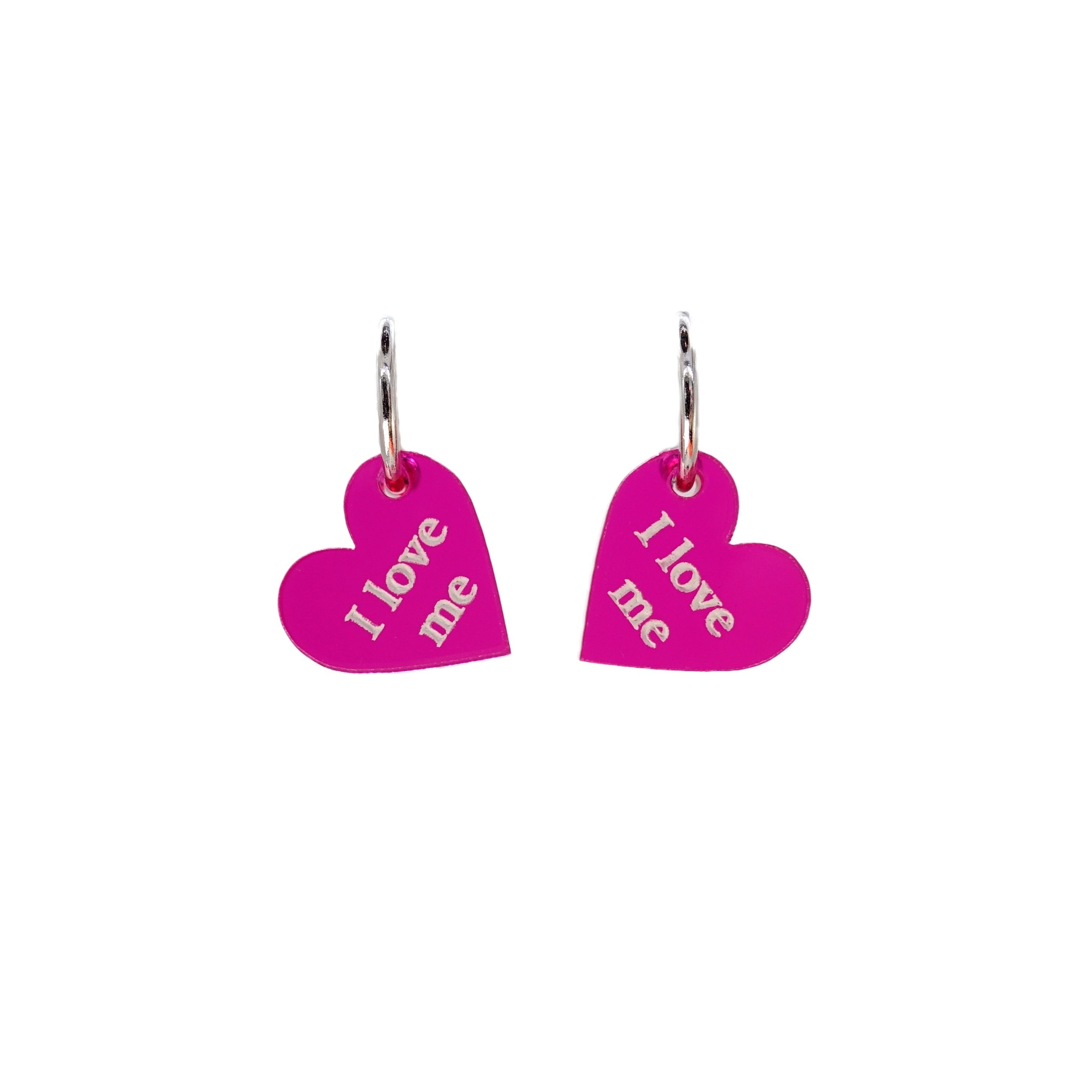 Small heart hoop earrings in neon pink, etched with the words 'I love me' on silver plated hoops, shown against a white background. 