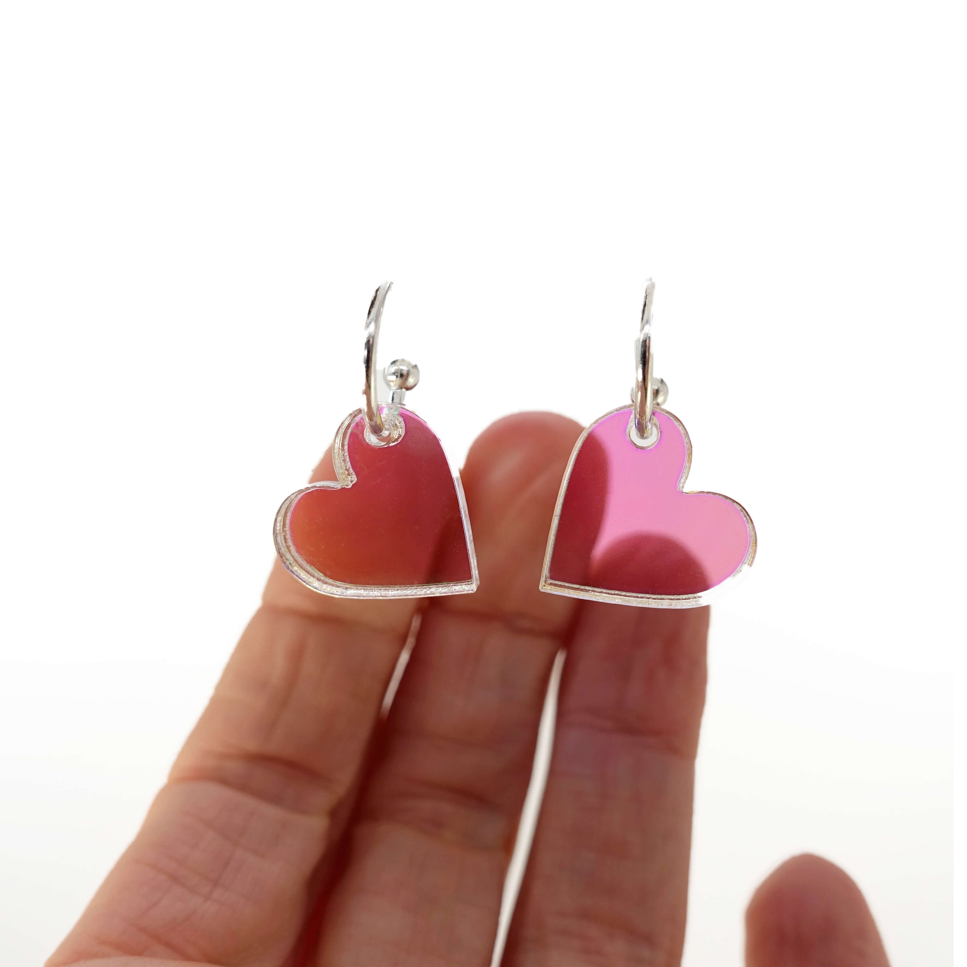 Iridescent simple heart hoop earrings hanging with a hand behind to show their transparence/iridescence. 