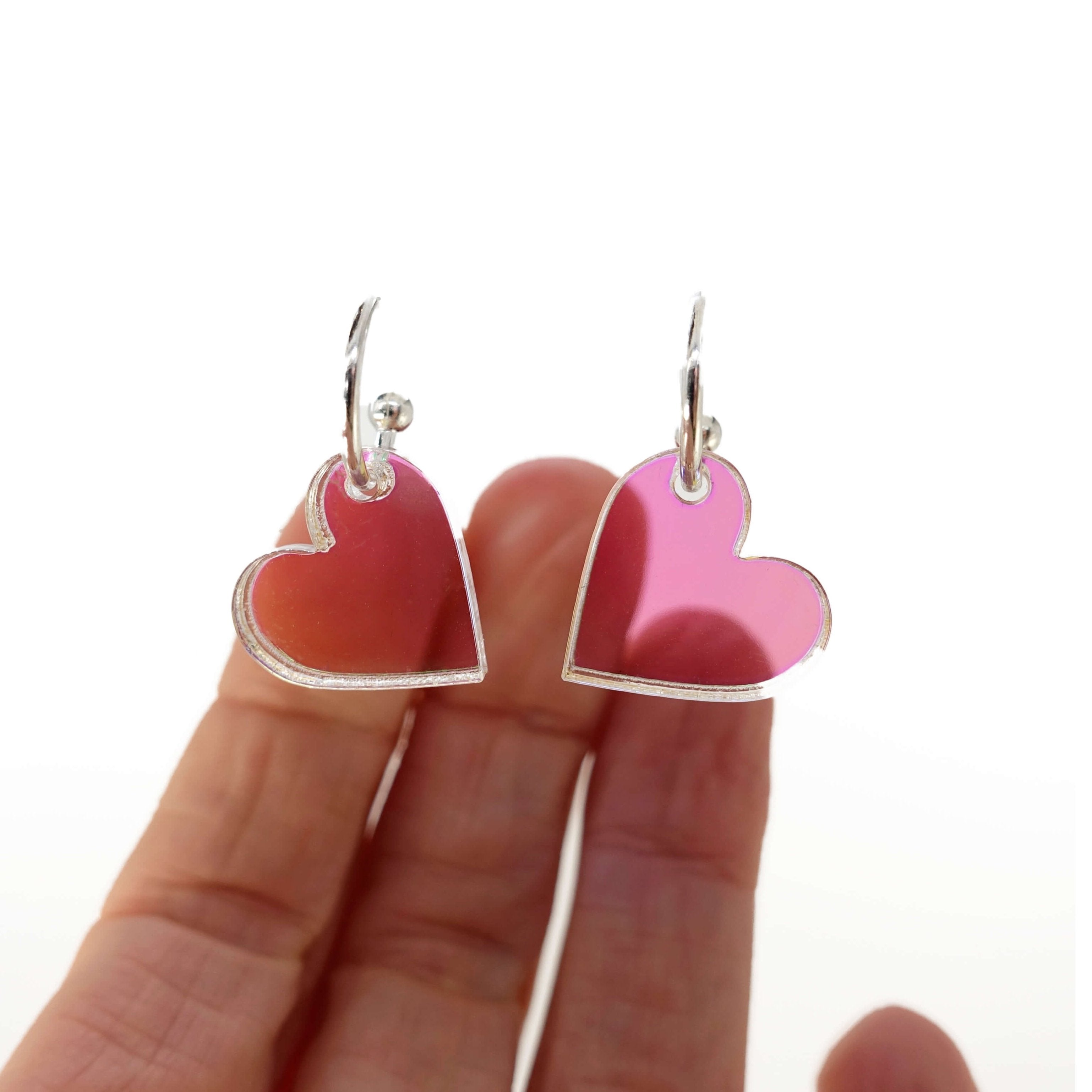 Iridescent simple heart hoop earrings on silver-plated hoops. Shown hanging against a white background with my fingers behind for scale and to show the transparency of the iridescent acrylic. 