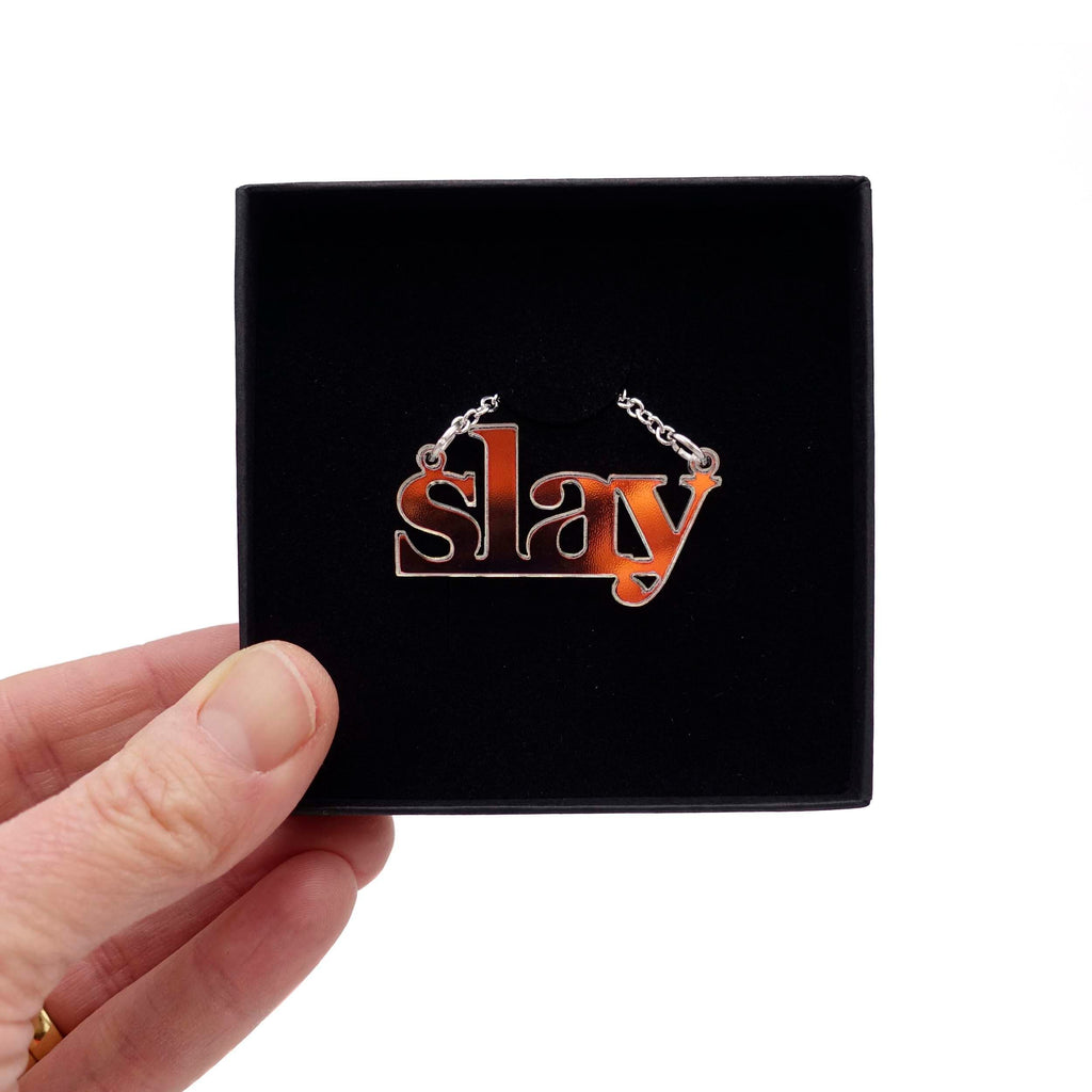 Iridescent Slay necklace shown being held up in a Wear and Resist gift box. 