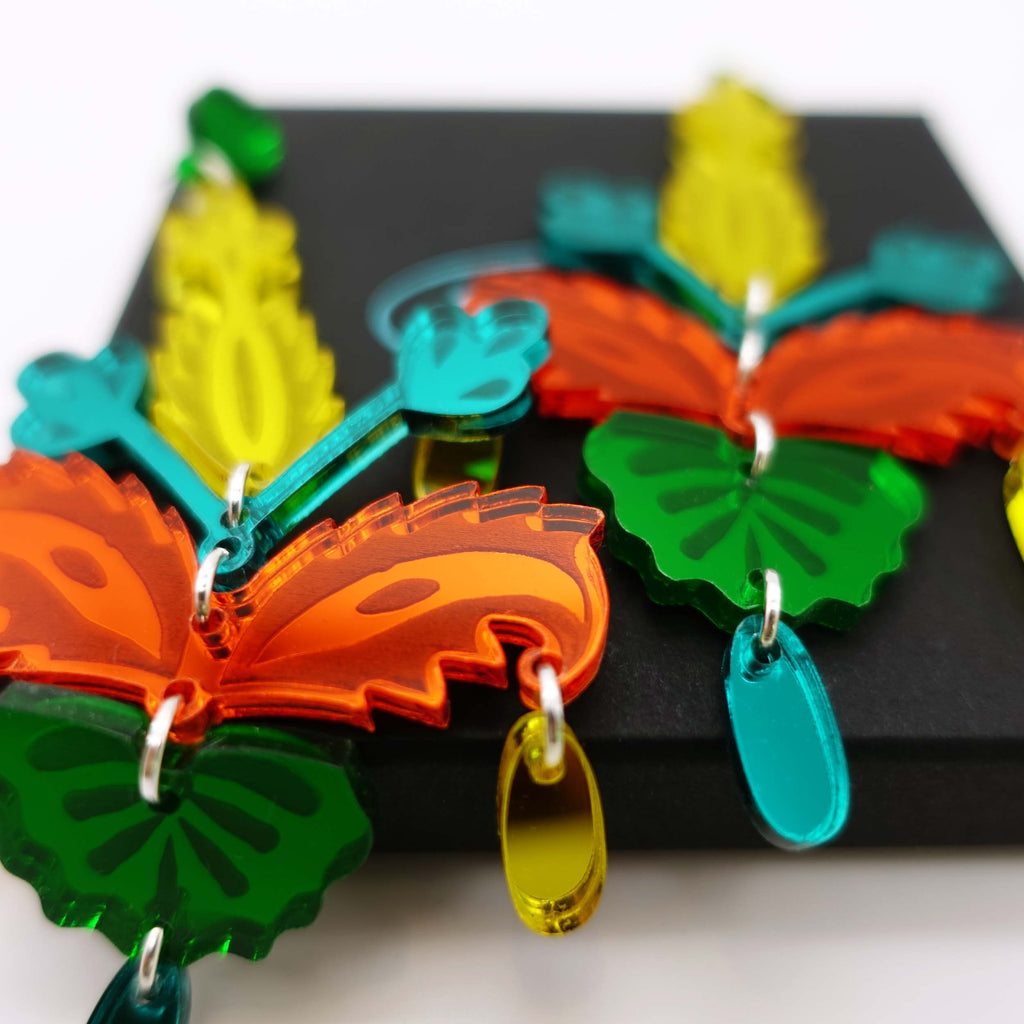 Close up of yellow, teal, orange and green Mambo Festival  earrings in shiny mirror acrylic, designed by Sarah Day for Wear and Resist.  Earrings for going out out and partying in the sun! 